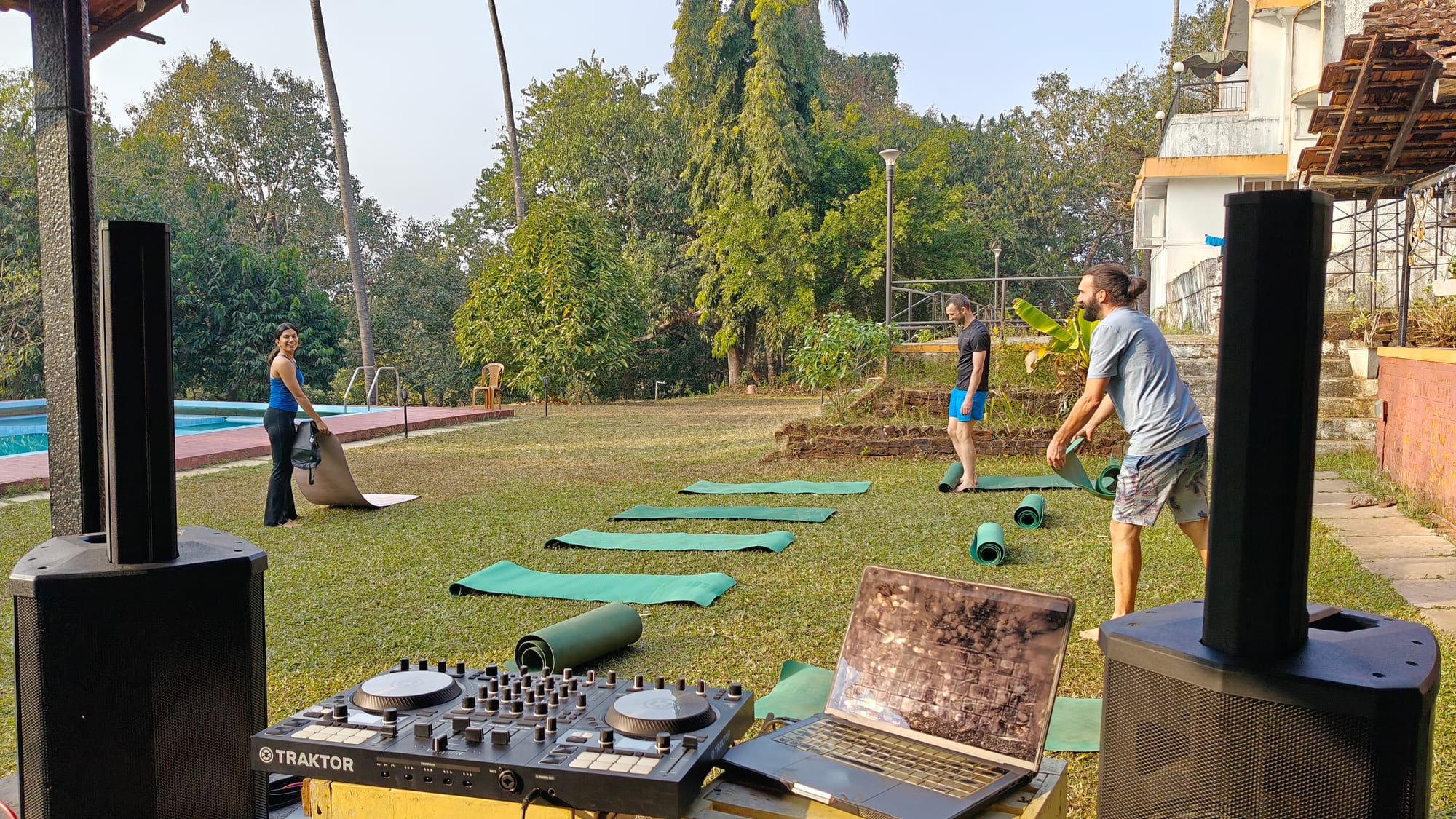 Decks and speakers set up on the lawn while yoga mats are rolled out by the pool