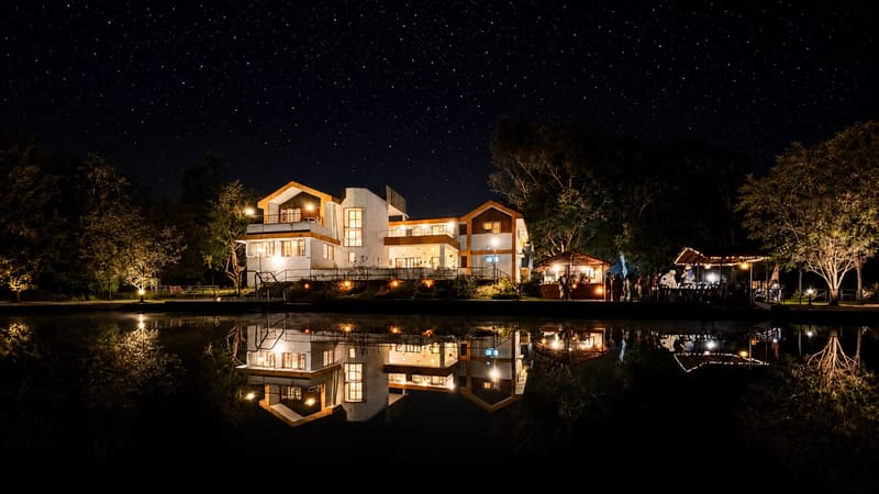 The lit Jungli bungalow mirrored in the pond under a sky full of stars