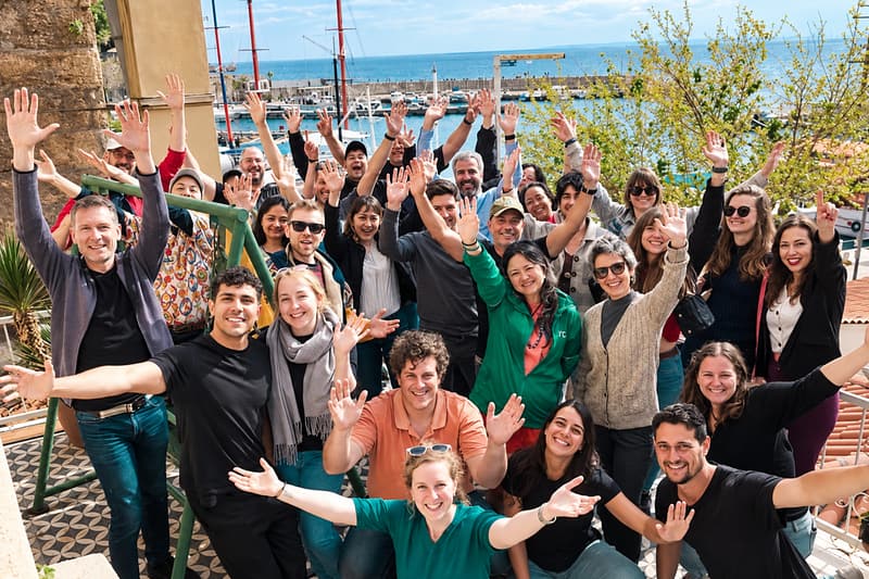 A large group of digital nomads with their arms in the air by the water